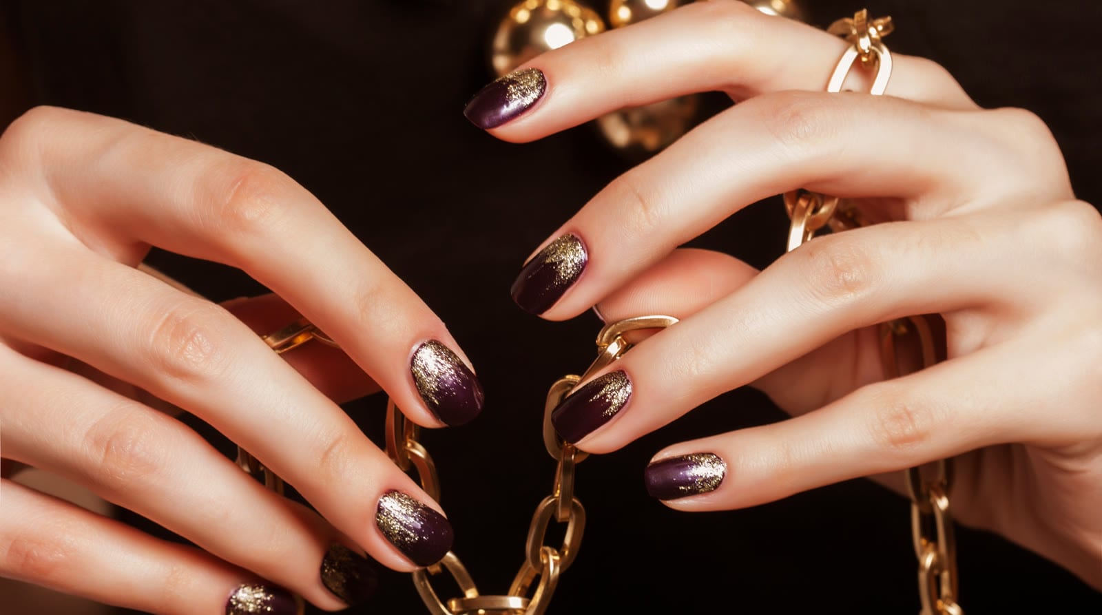 Plum nails with gold glitter tips, holding a gold chain