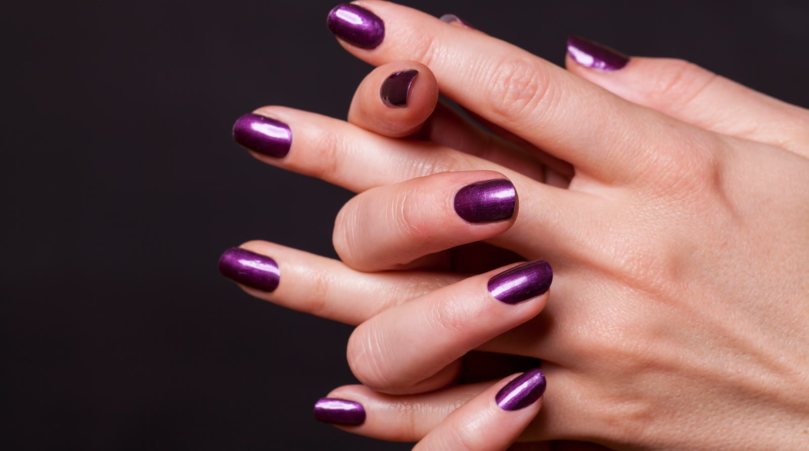Hands crossed to show a metallic violet manicure